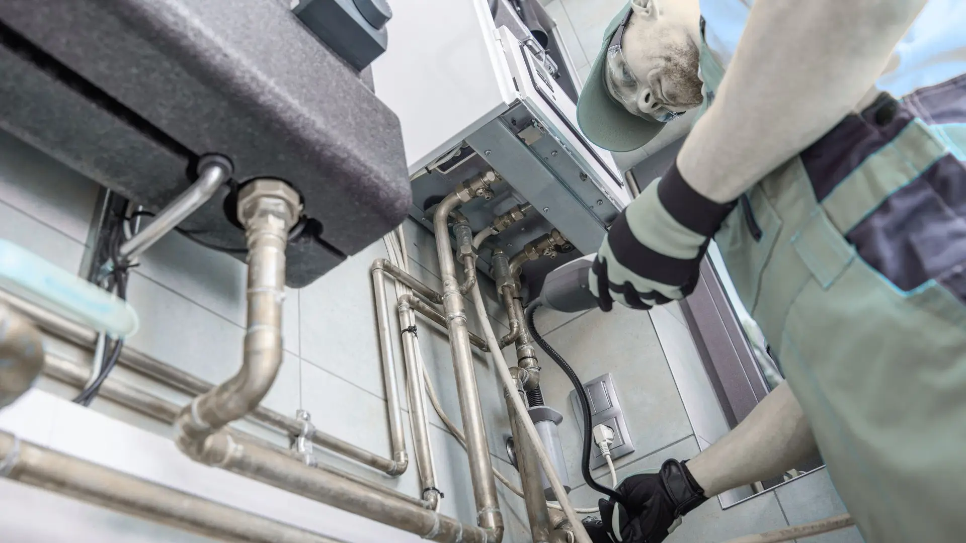 Technician inspecting heating system pipes under boiler