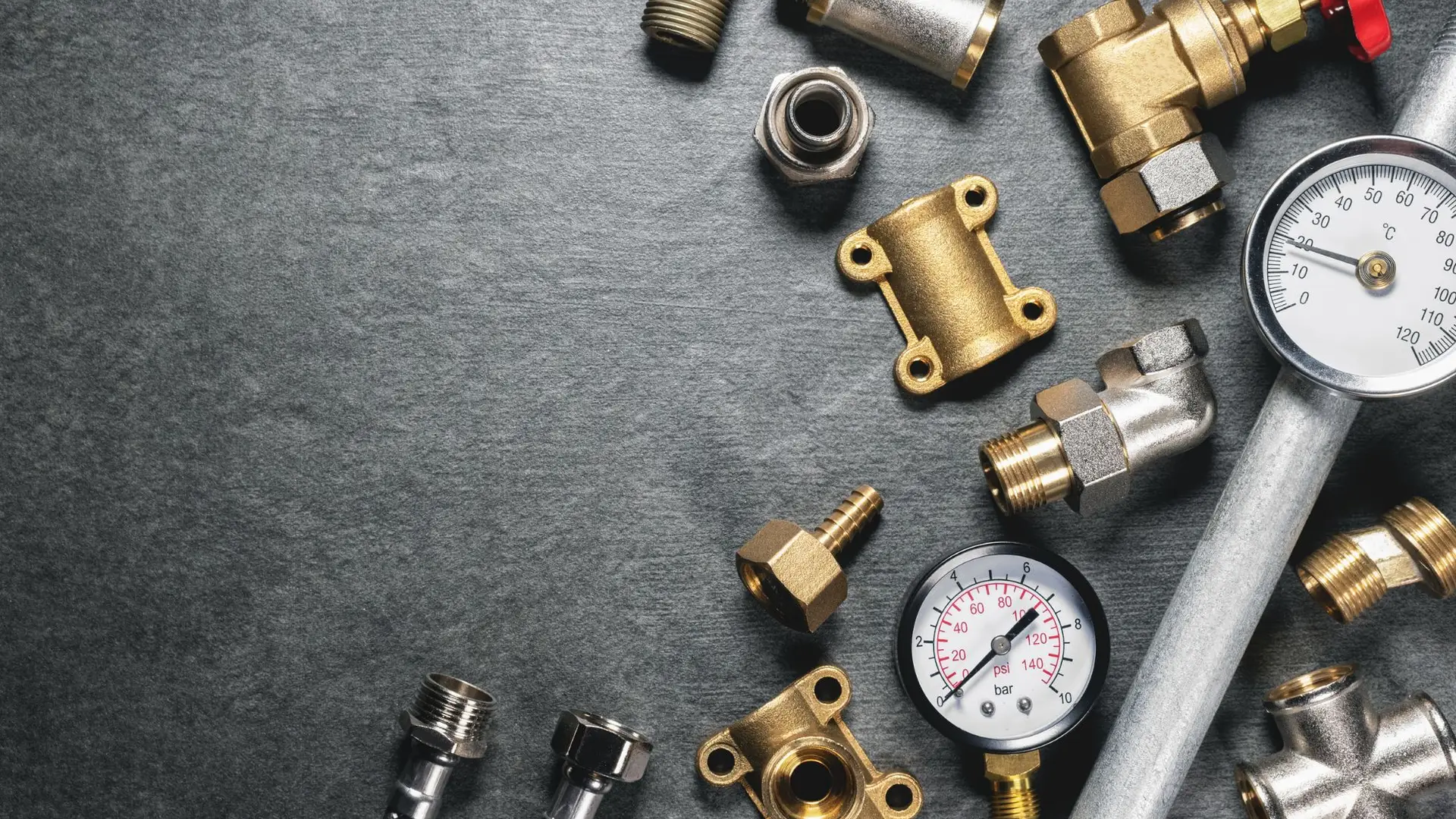 Assorted plumbing fittings and pressure gauge on gray background.