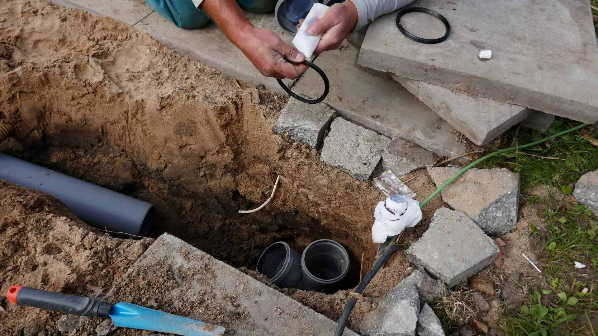 Person installing outdoor drainage pipes in a trench.