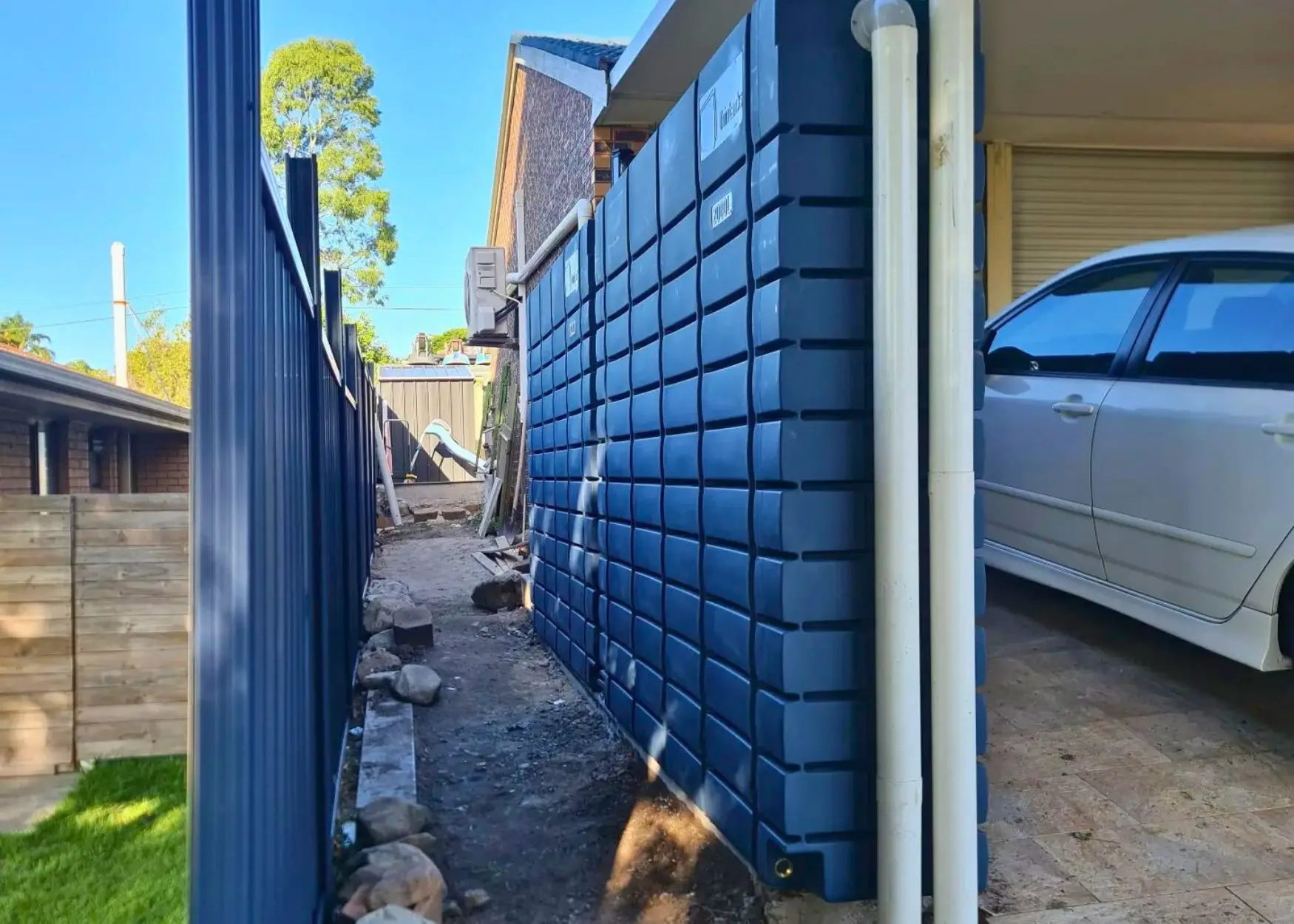 Narrow pathway with blue rainwater tank and car.