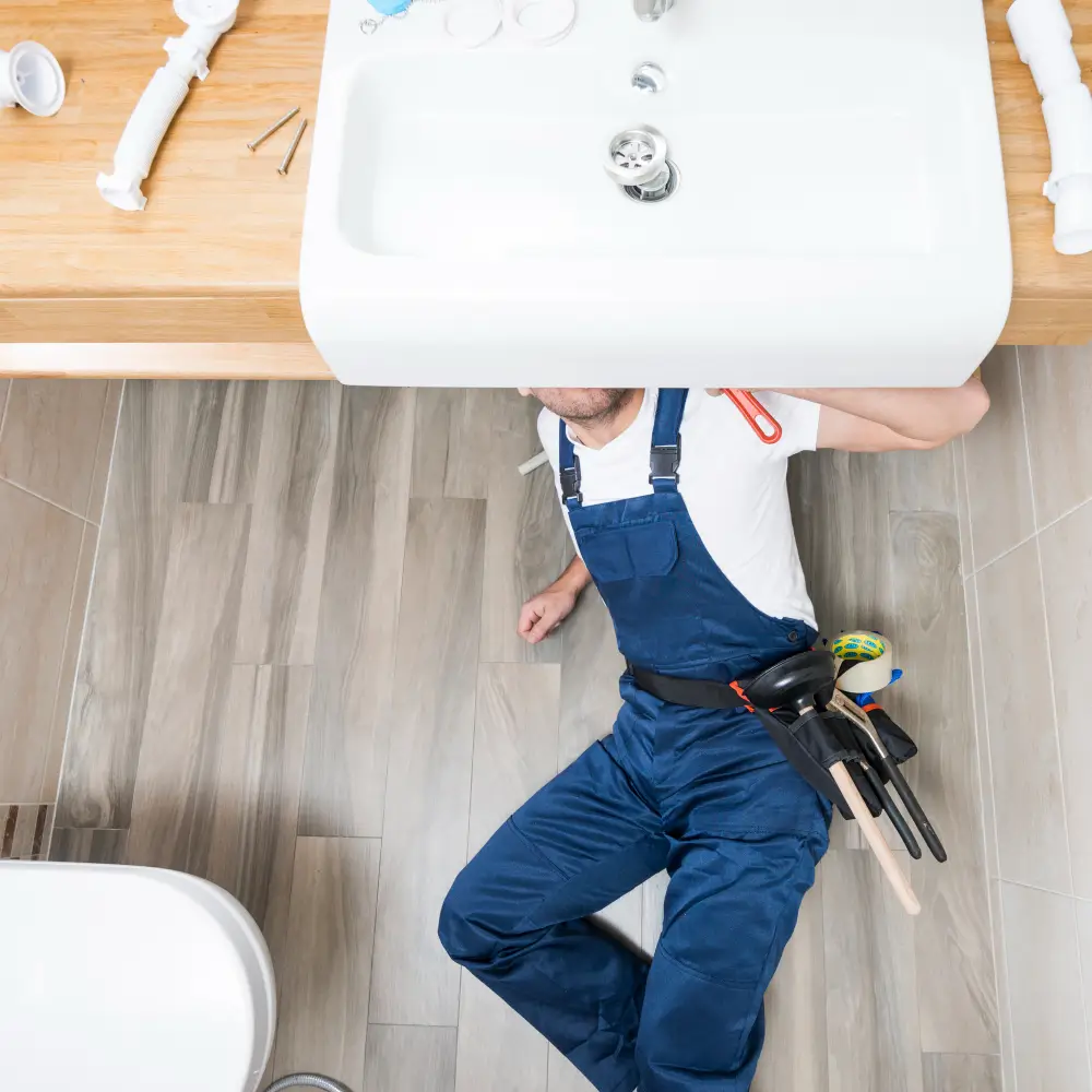 Plumber fixing sink with tools under counter.