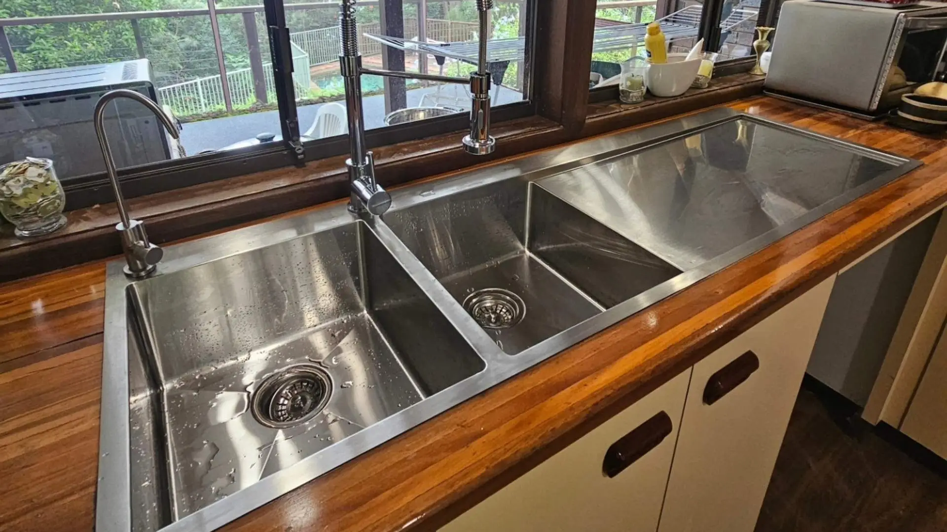 Stainless steel double kitchen sink with wooden counter.
