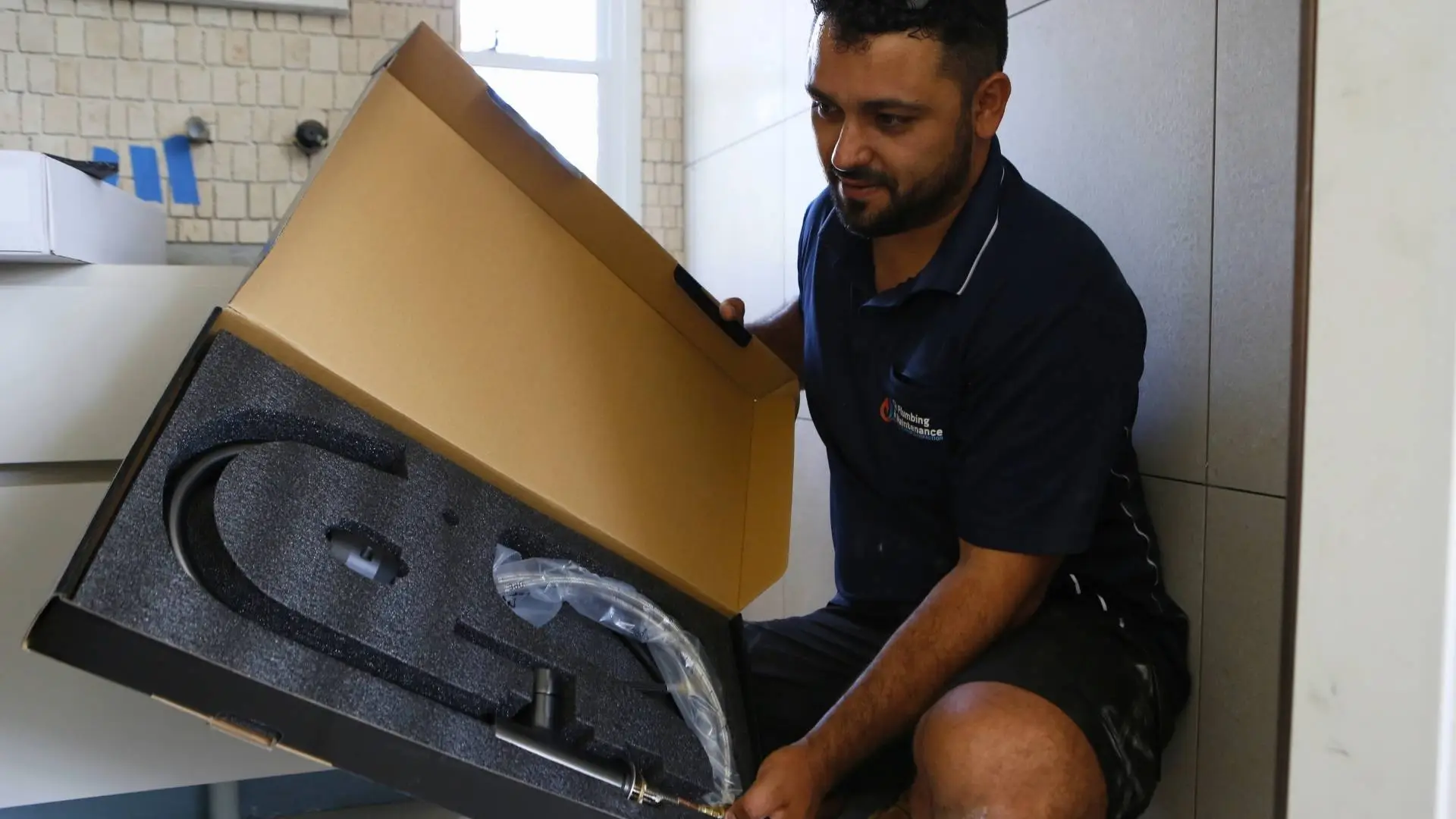 Plumber examines boxed sink parts for installation.