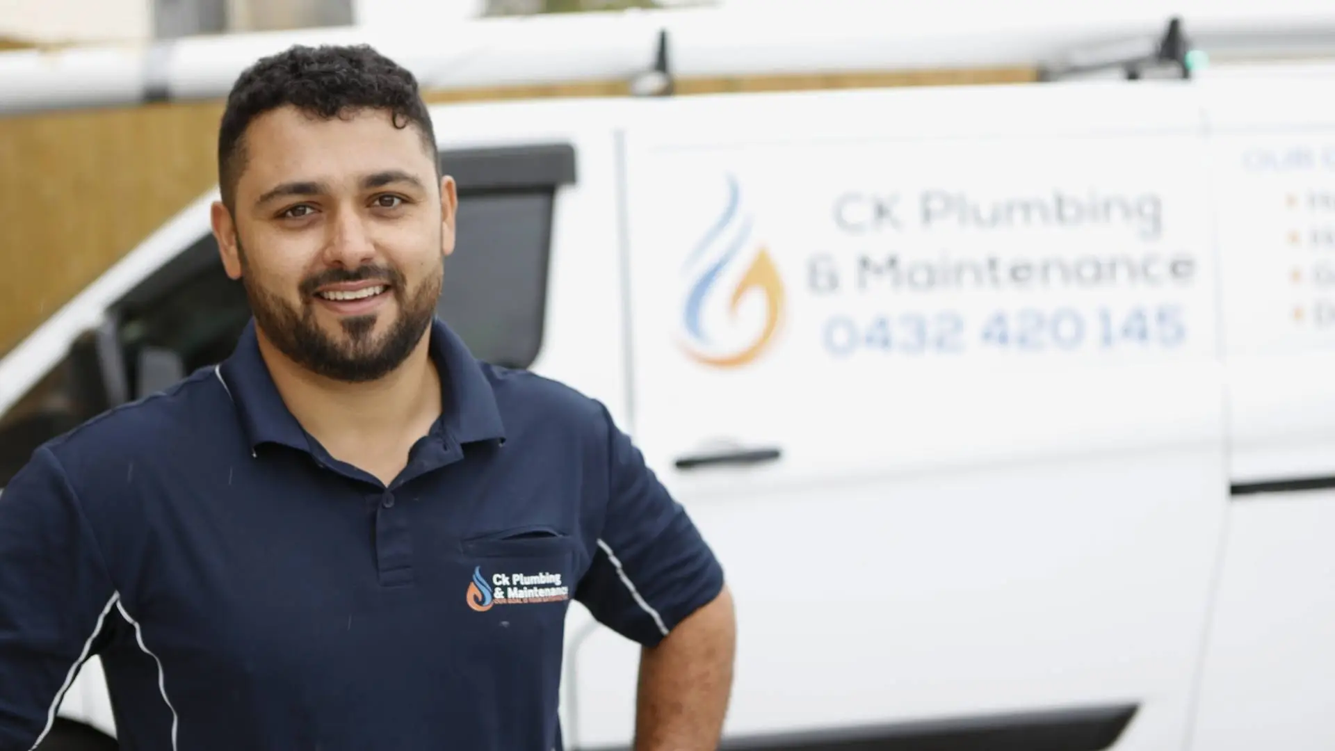 Smiling plumber standing by company van.