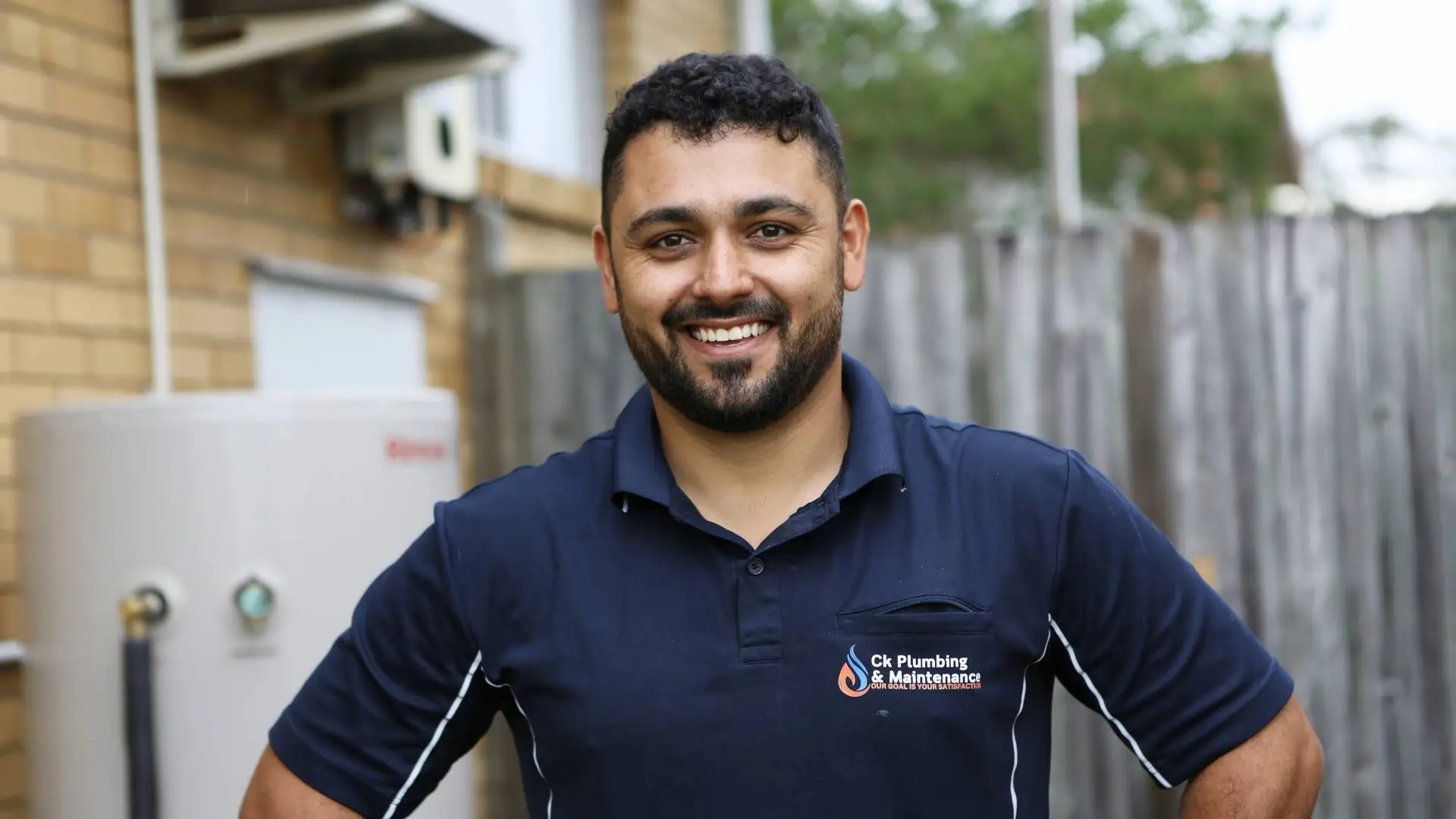 Smiling plumber in uniform outside a building.