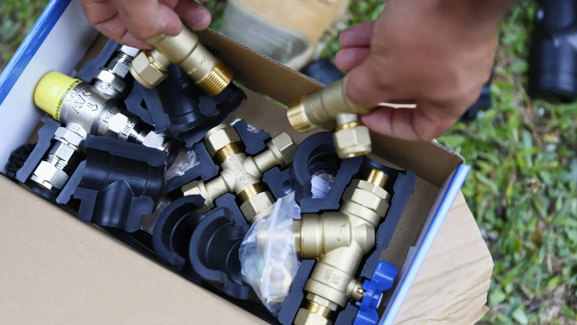Box of metallic pipe fittings being examined.